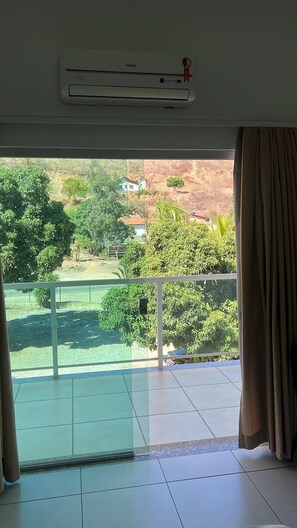 Una habitación con vistas a un paisaje verde, un balcón con puerta de cristal y un equipo de aire acondicionado en la pared.