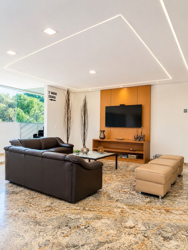 Una sala moderna con sofá, reposapiés, mesa de centro y un televisor de pantalla plana montado en un mueble de madera.