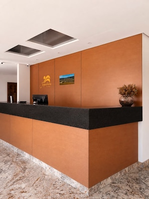 Una recepción de hotel con un logotipo, una máquina de café y un jarrón con flores secas.