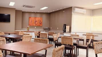 A dining area with tables and chairs, a flat-screen TV mounted on the wall, and an air conditioning unit.