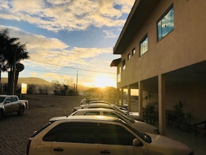 Un área de estacionamiento con coches aparcados frente a un edificio de techo plano y varias ventanas.