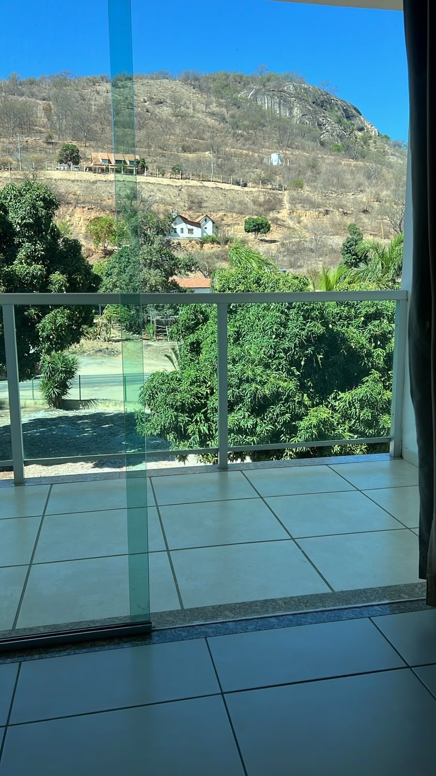A balcony with a view of a hillside, a small house, and some greenery.