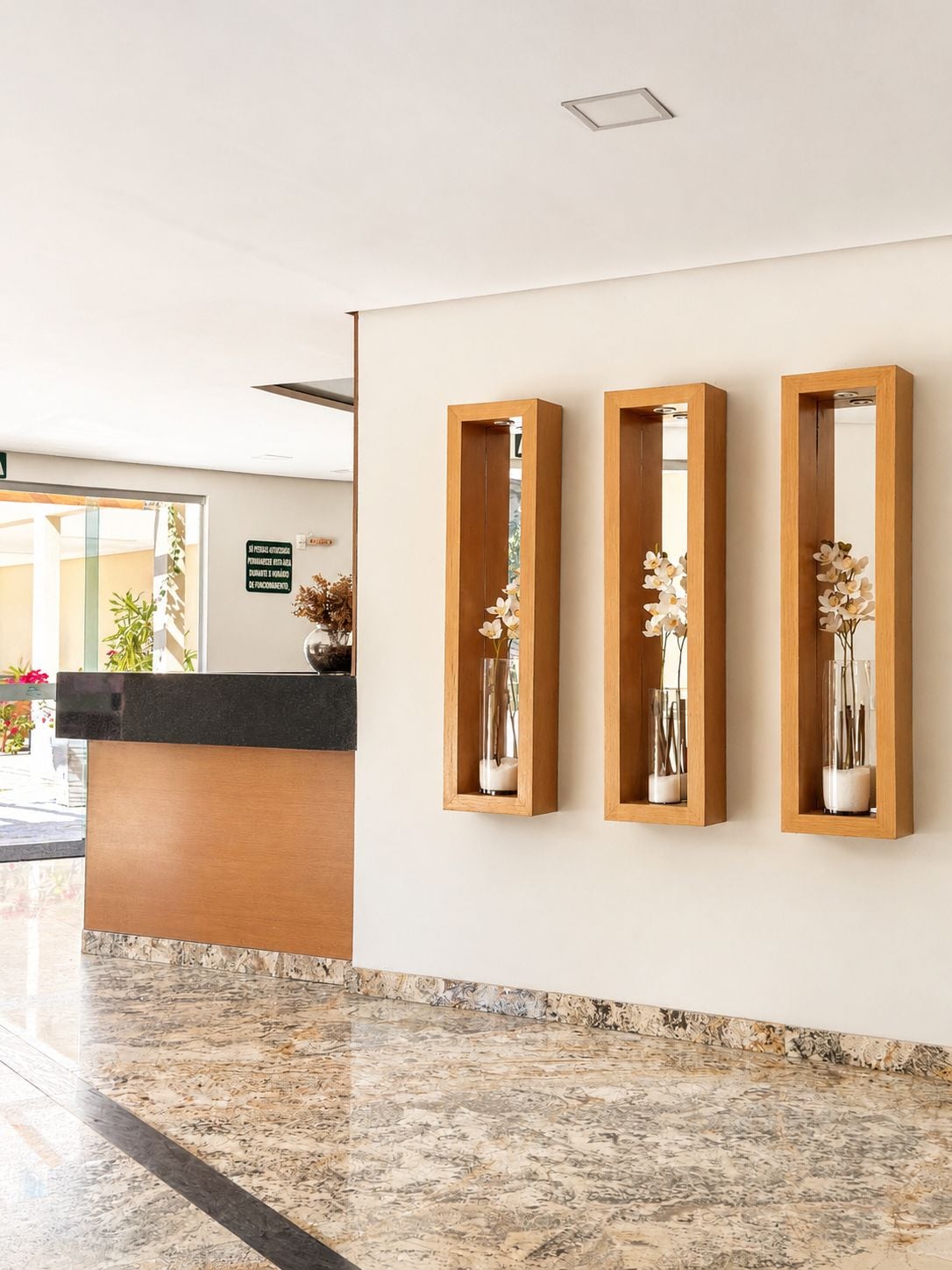 A reception area with a marble floor, a reception desk, and three wooden-framed mirrors with vases of flowers.