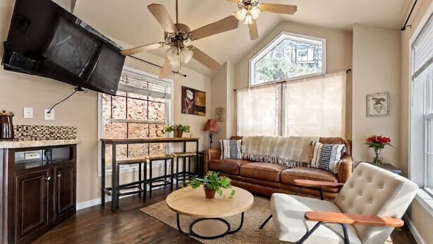 A living room with a ceiling fan, a TV mounted on the wall, a sofa, a coffee table, and a dining area with a table and chairs. - Woodland Peak Tiny Lodge (Woodland Park)