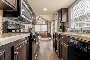 A kitchen with dark wooden cabinets, a stainless steel stove, and a dishwasher. - Woodland Peak Tiny Lodge (Woodland Park)