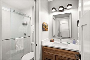 A modern bathroom with a glass shower enclosure, a white sink, and a large mirror with three lights. - RiverWest Trailside Tranquility - Sauna - Dogs Friendly (Duluth)