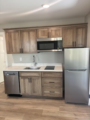 A kitchen with wooden cabinets, a stainless steel microwave, a refrigerator, and a dishwasher. - RiverWest Trailside Tranquility - Sauna - Dogs Friendly (Duluth)