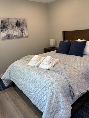 A neatly made bed with a quilted cover, two pillows, and folded towels. - RiverWest Trailside Tranquility - Sauna - Dogs Friendly (Duluth)