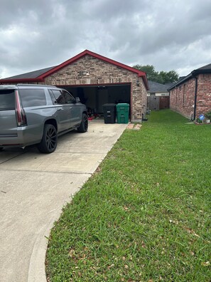 Eine Garage mit Ziegelaußenwand, einem geparkten SUV und zwei Mülltonnen.
