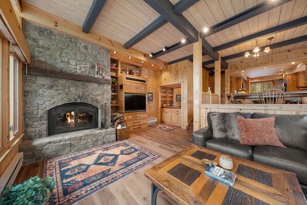 A cozy living room with a stone fireplace, wooden beams, and a leather sofa.