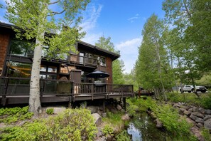 Ein zweistöckiges Gebäude mit einer Terrasse, einer kleinen Sitzgelegenheit im Freien und einem Teich.