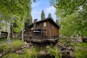 Una baita in legno a due piani con un balcone, circondata da alberi e rocce.