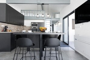 A modern kitchen with dark cabinets, a central island with stools, pendant lighting, and a large window. - Cozy Cottage with Spa - Welkeys (Moliets-et-Maa)