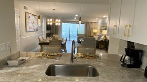 A modern kitchen with a central island, stainless steel sink, and dining area with chairs and tables. - Magical Disney Getaway: 2-Bed Villa with Loft at Premier Water Park Resort! (Kissimmee)