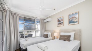 A hotel room with two beds, a ceiling fan, air conditioning, a window with curtains, and two framed pictures on the wall. - Heart of Townsville on the Harbour (Townsville City)
