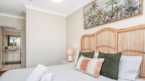 A bedroom with a bed, pillows, a bedside table with a lamp, a mirror, and a bathroom visible through an open door. - Heart of Townsville on the Harbour (Townsville City)