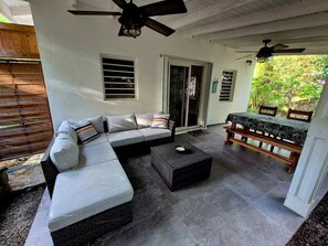 Eine überdachte Terrasse mit einem Ecksofa, einem Esstisch mit Bänken und einem Deckenventilator.