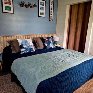 Uma cama com colcha azul e branca, cabeceira de madeira e várias almofadas.