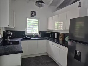 Eine moderne Küche mit weißen Schränken, einem Edelstahl-Kühlschrank, einer Kaffeemaschine und einem Fenster mit Jalousien.