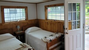 A room with two beds, a wooden door, and a window with blinds.