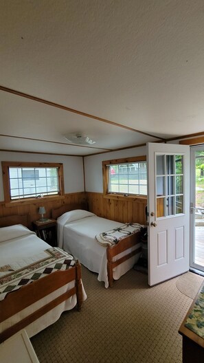 A room with two beds, a wooden door, and a window with blinds.