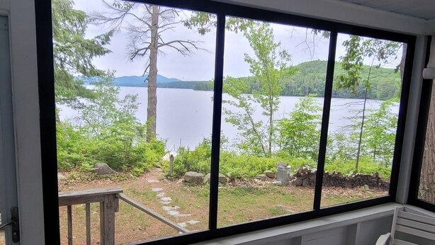 A room with a large window overlooking a lake, a wooden bench, and a table.