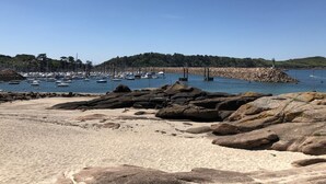 A beach with rocky foreground, clear blue sky, and a marina with boats. - Ker Lann - TREBEURDEN (TREBEURDEN)