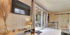 Een modern interieur met een flatscreen-tv, een houten boekenkast, een eethoek met tafel en stoelen, en een schuifdeur naar buiten.