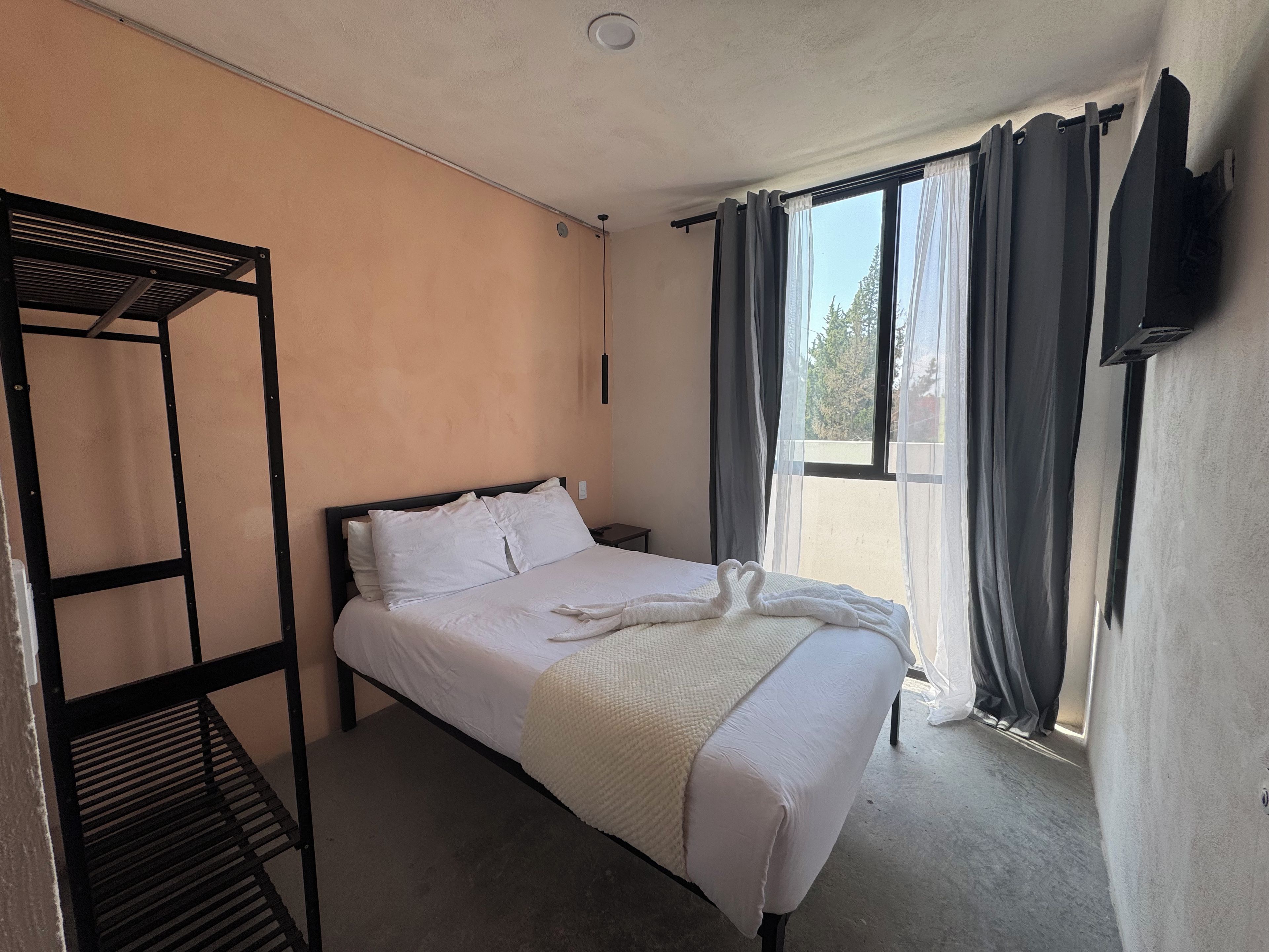 A single bed with white bedding, a black metal frame, a bedside table, and a window with curtains.
