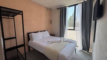A single bed with white bedding, a black metal frame, a bedside table, and a window with curtains.