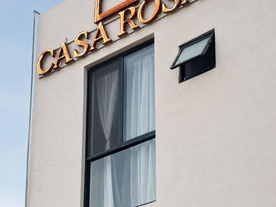 Un edificio con un cartel que dice 'CASA ROSA' y dos ventanas con cortinas.