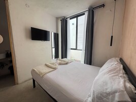 Ένα δωμάτιο ξενοδοχείου με ένα κρεβάτι, μια τηλεόραση τοποθετημένη στον τοίχο και ένα παράθυρο με κουρτίνες.