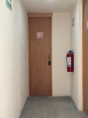 A hallway with a wooden door marked '05', a fire extinguisher on the wall, and a small sign indicating a smoking area.