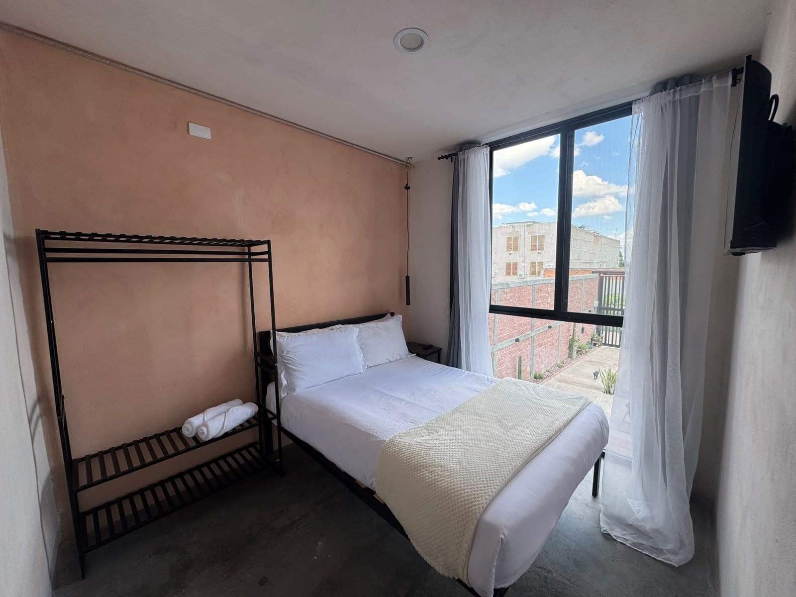 A bedroom with a bunk bed, a single bed, a window with curtains, and a TV mounted on the wall.