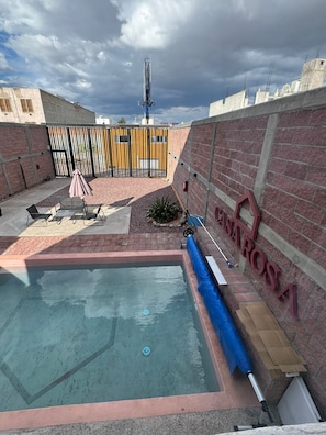 Una piscina con una cubierta azul, un muro de ladrillo y una reja de metal.