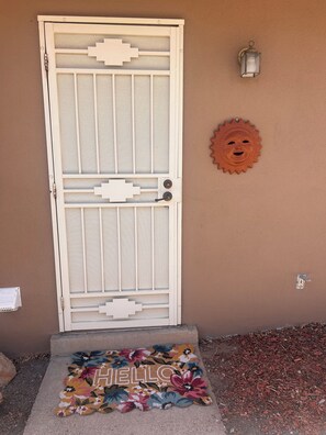 A door with a metal grill, a wall-mounted light fixture, and a welcome mat with 'HELLO' on it.
