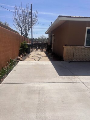A concrete pathway leading to a gated area with a dog, a fence, and a building with a brick base.