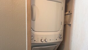 Una lavadora y secadora compacta, de color blanco, con carga frontal y panel de control que muestra ajustes de temperatura y ciclo.