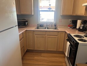A kitchen with wooden cabinets, a double sink, a microwave, a stove, and a window with a view of the outside.