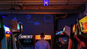 A person standing between arcade machines with neon signs, including 'ALPINE SKI' and 'FUNKY.'