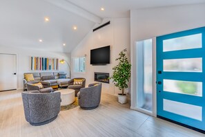 A modern living room with a fireplace, a flat-screen TV, and a blue door. - Sun and Games - Stylish Desert Retreat (Palm Springs)