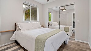A bedroom with two beds, a ceiling fan, a large mirror, and a window.