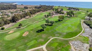 A golf course with a coastal view, sand bunkers, and a clear sky.