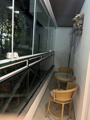 Ein Balkon mit Glastrennwand, zwei Korbstühle und ein kleiner Tisch.