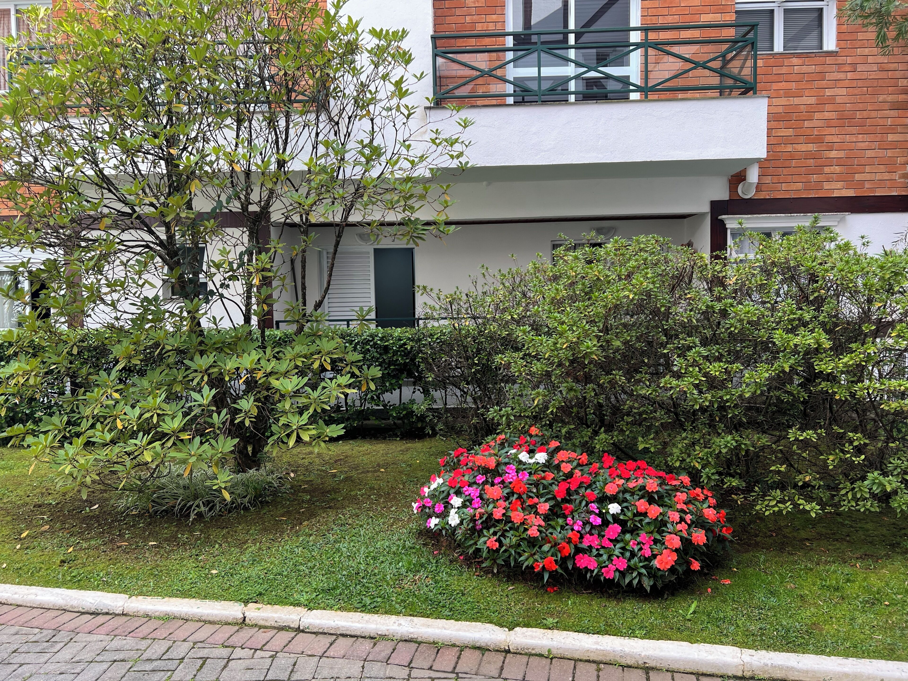 A residential building with a balcony, a well-maintained garden with various shrubs and a flower bed.