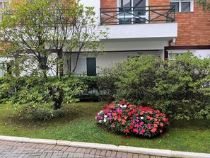 Ein Wohngebäude mit Balkon, ein gepflegter Garten mit verschiedenen Sträuchern und einem Blumenbeet.