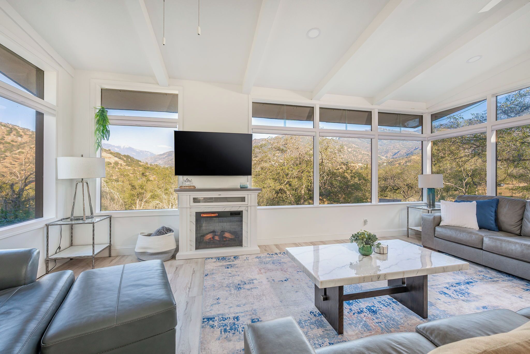 Una sala de estar moderna con chimenea, televisor de pantalla plana y un amplio ventanal con vistas a la montaña.