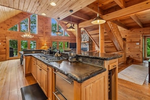 Un intérieur de chalet spacieux, avec des murs en bois, un grand îlot de cuisine, des appareils électroménagers intégrés et un mur d’accent en pierre.