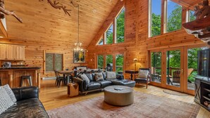 A spacious log cabin interior with a dining area, a leather sofa, and a large window overlooking greenery. - Escape to Summit View Lodge in Mountaintop, a spacious pet-friendly retreat for 14! (McHenry)