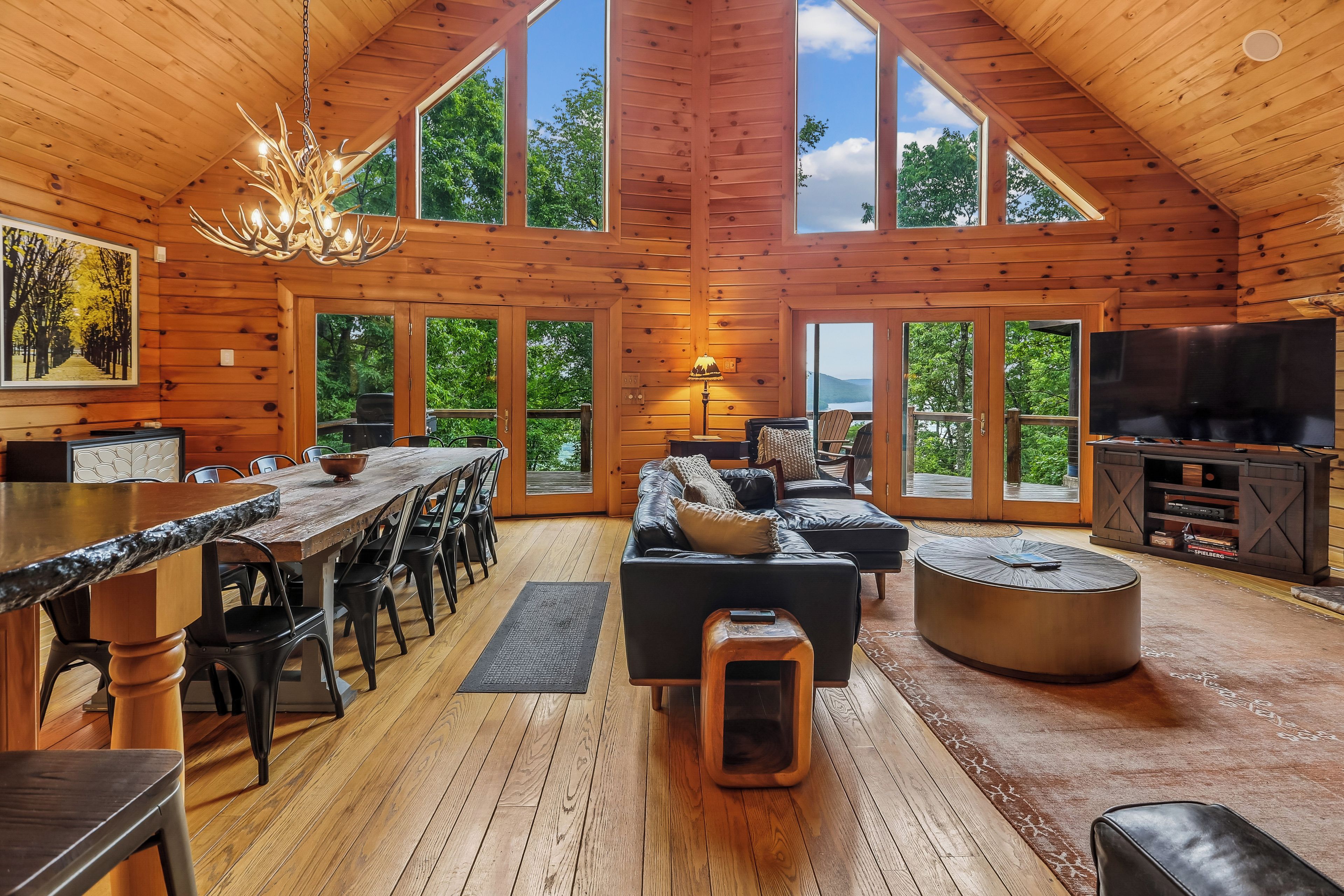 A spacious wooden cabin with a dining area, living room, and large windows offering views of the outdoors.